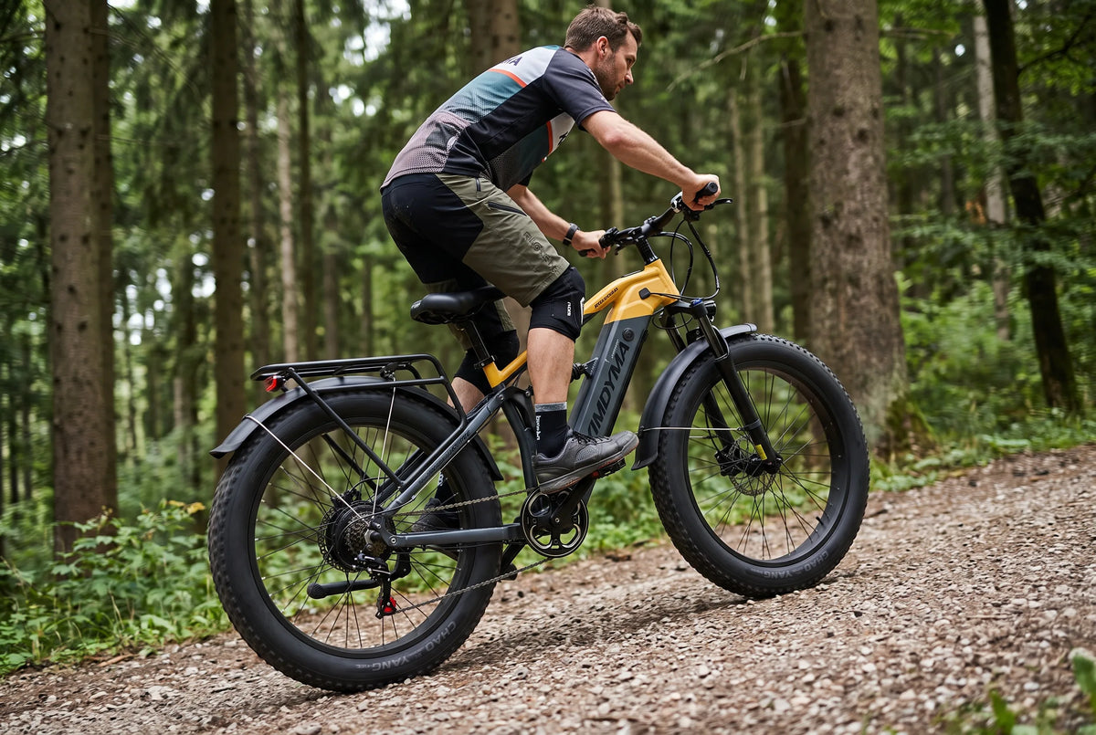 Ciclista con rodilleras en una bicicleta eléctrica de montaña subiendo por un sendero forestal de grava