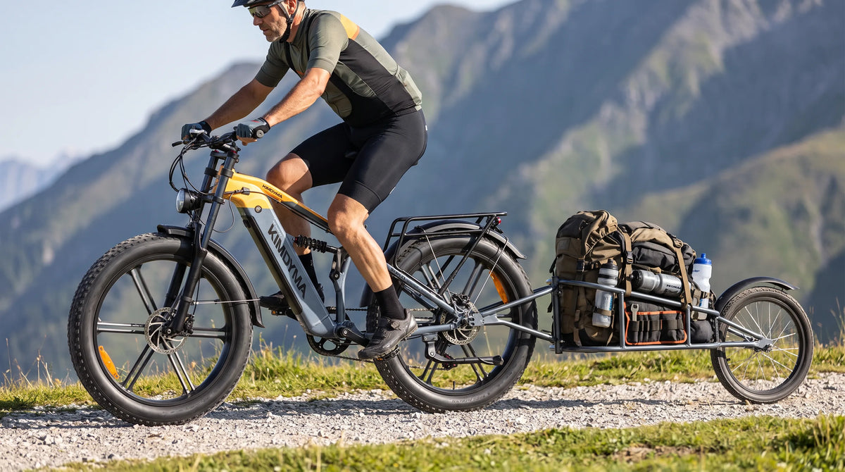 Ciclista masculino de bicicleta eléctrica de gravel remolcando un remolque de una sola rueda en una carretera de grava alpina, luz de la mañana, telón de fondo de montaña