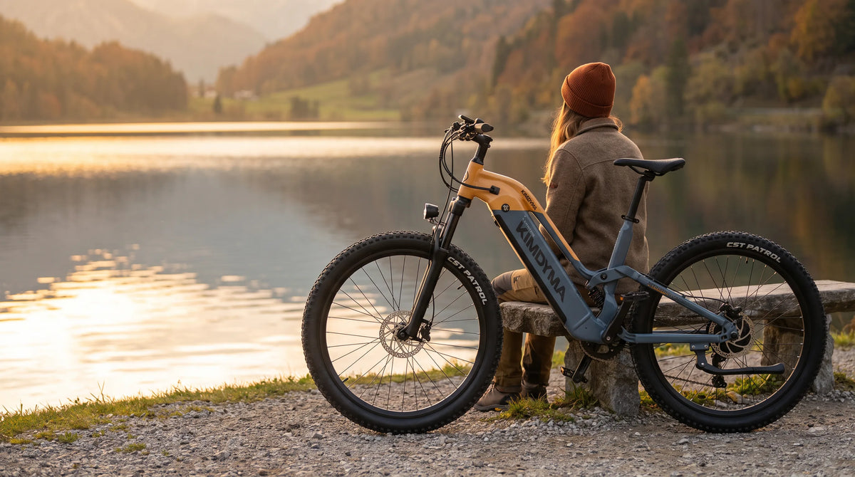 Una mujer sentada de espaldas a nosotros en un banco de piedra junto a un lago, con una bicicleta eléctrica Kimdyma K02 aparcada detrás de ella en otoño.