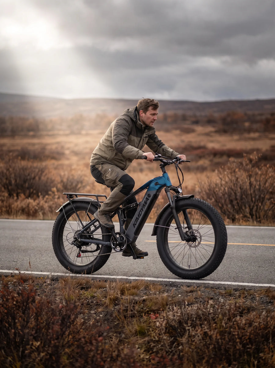 Rowerzysta na rowerze elektrycznym typu fat-bike Kimdyma K05 jadący wzdłuż krawędzi pustej drogi przez otwarte jesienne wrzosowiska.
