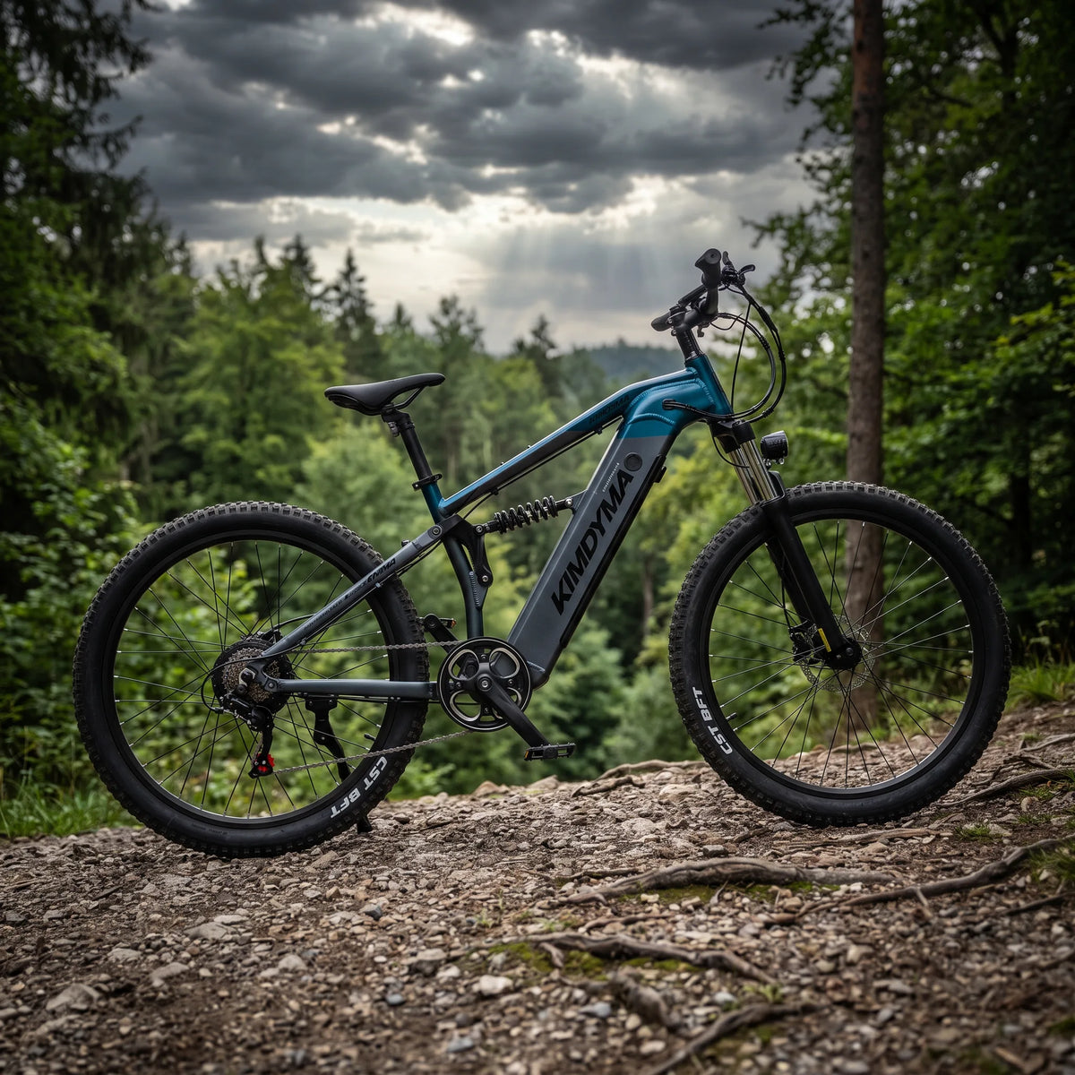 Primo piano dell'ammortizzatore posteriore su una bici elettrica Kimdyma M1 ARETE parcheggiata su un sentiero boschivo roccioso.