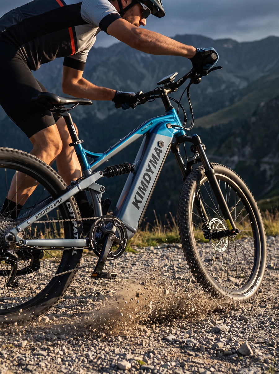 A cyclist riding a Kimdyma K01 e-bike at speed on a rough gravel mountain trail, with dust and small stones kicked up by