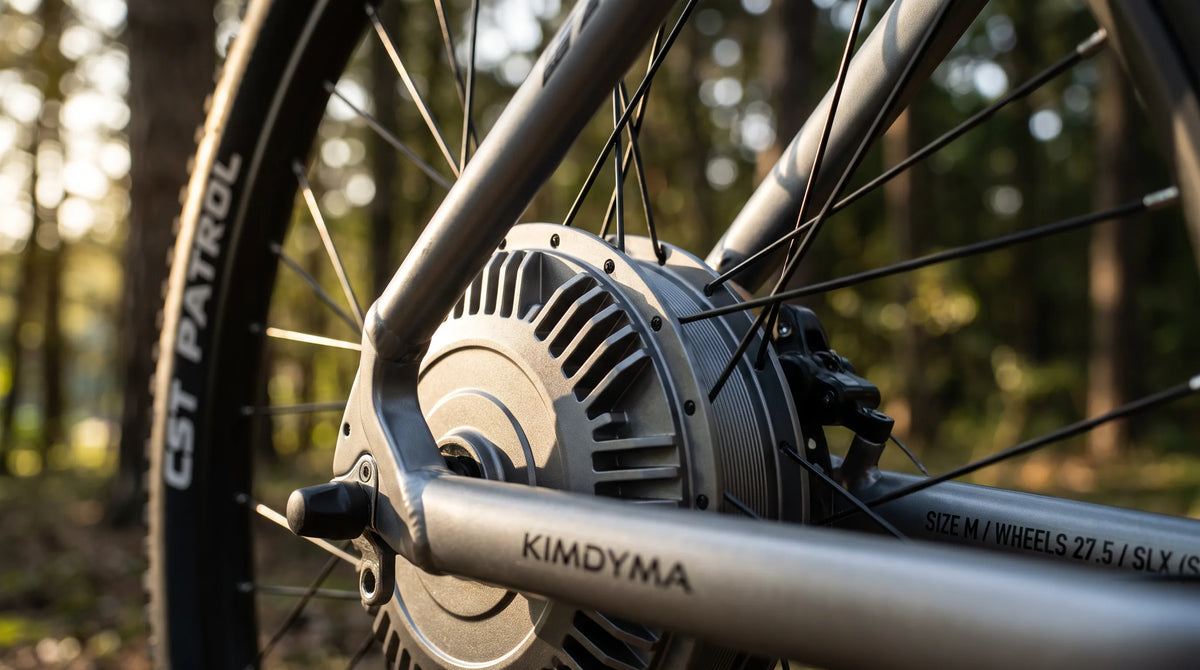 Nahaufnahme des Nabenmotors am Hinterrad eines Kimdyma E-Mountainbikes auf einem schlammigen Pfad, zeigt metallische Kühlrippen und mechanische Details mit bl