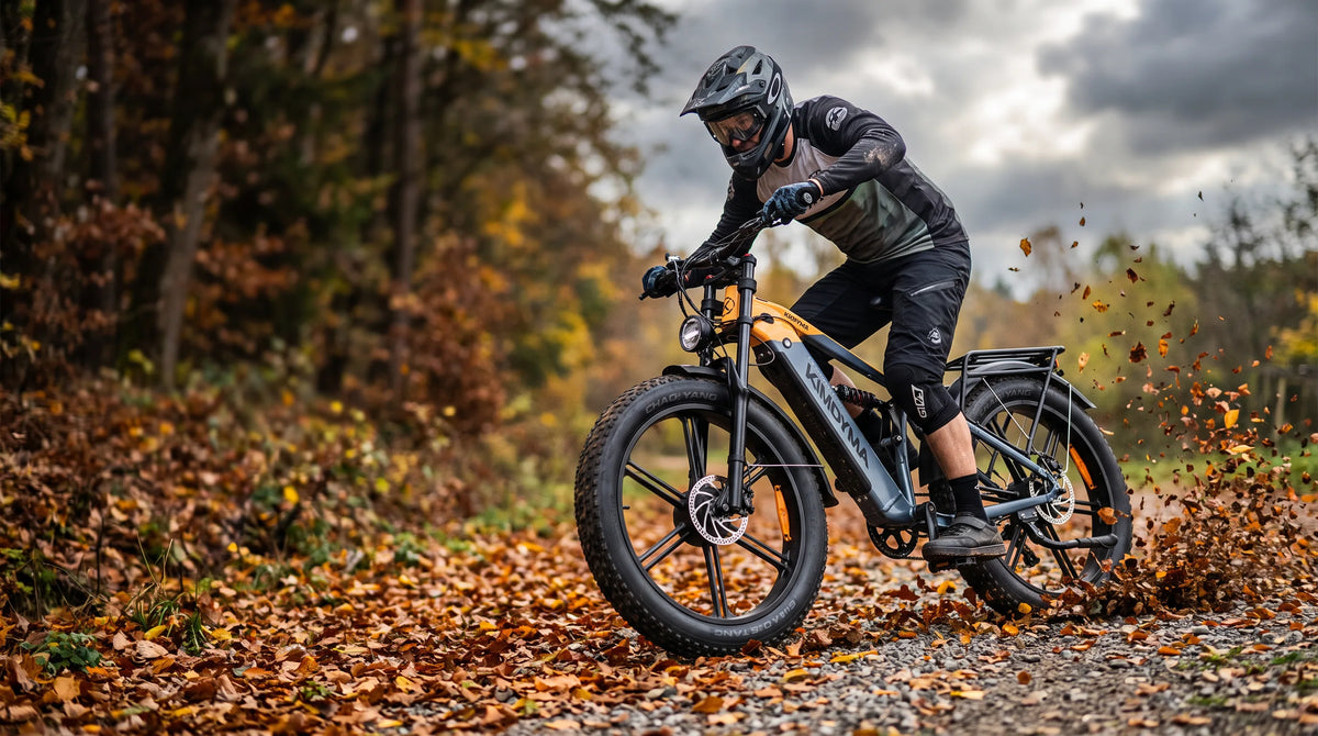 Bicicleta eléctrica de neumáticos anchos Kimdyma K03 circulando rápido por un sendero forestal de grava cubierto de hojas en otoño, levantando las hojas caídas.