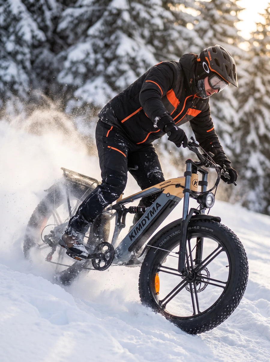 A cyclist riding a Kimdyma K03 e-bike downhill through deep snow in a mountain forest, with powder spraying from the wid
