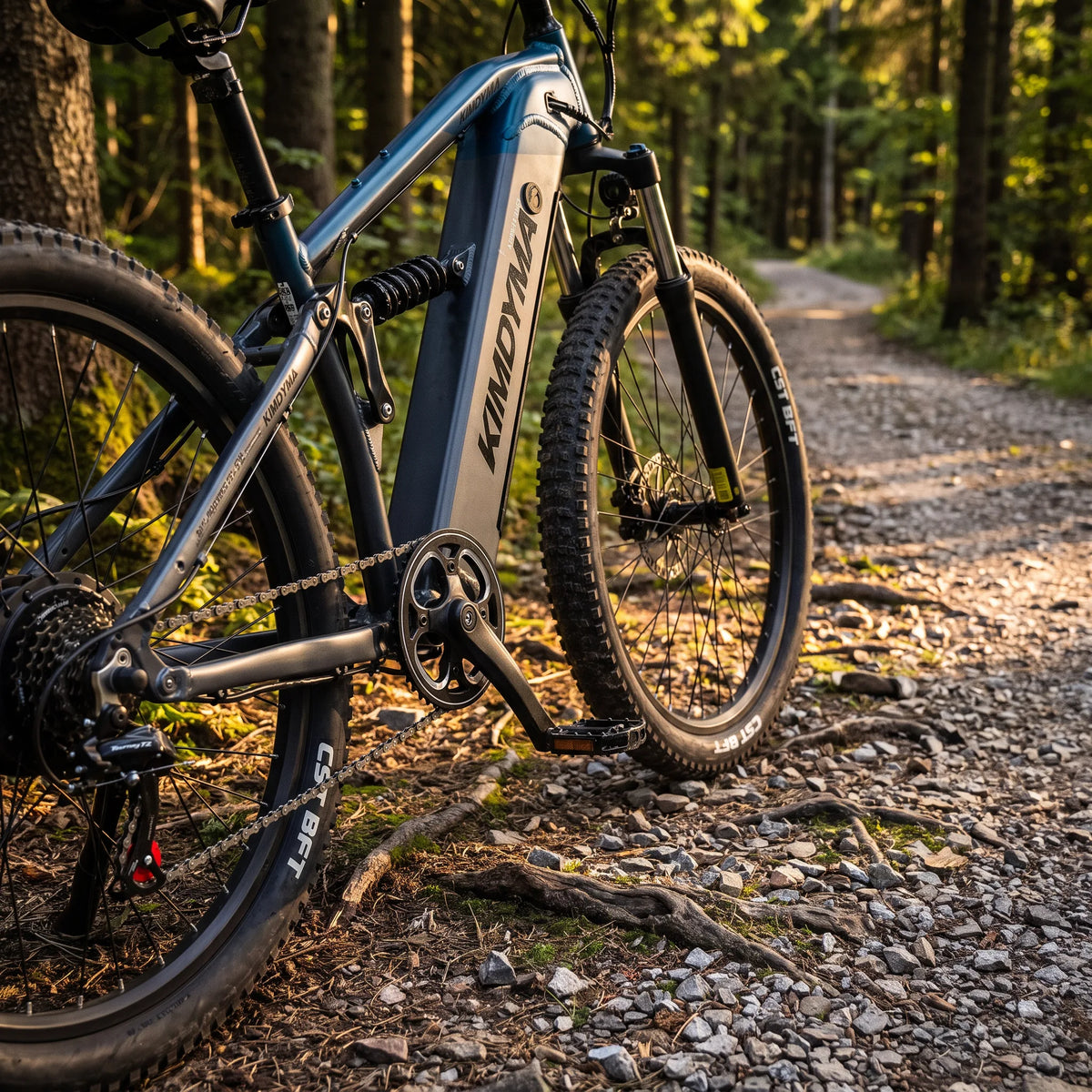 Una mountain bike elettrica Kimdyma con telaio blu scuro e pneumatici tassellati riposa su un sentiero in ghiaia attraverso un bosco soleggiato.