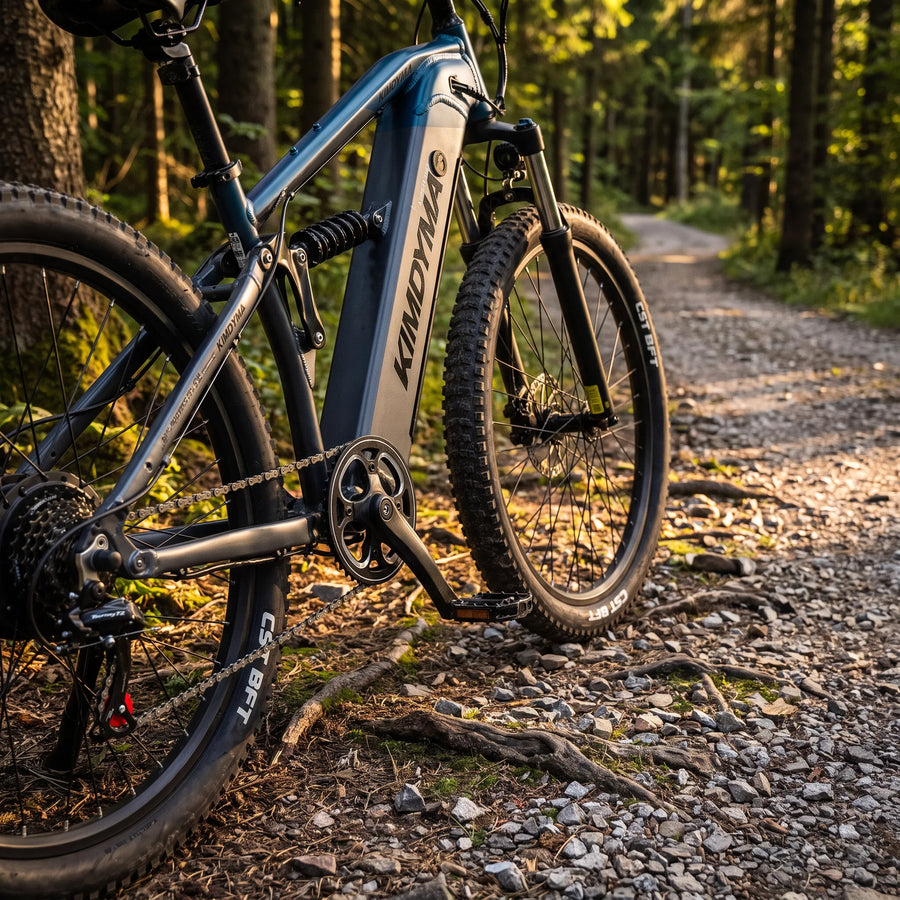 Una mountain bike elettrica Kimdyma con telaio blu scuro e pneumatici tassellati riposa su un sentiero in ghiaia attraverso un bosco soleggiato.