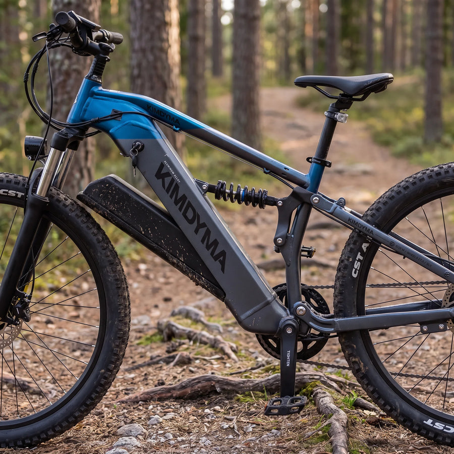 Una mountain bike elettrica Kimdyma blu e grigia con una grande batteria poggiata su un sentiero sterrato attraverso una pineta.